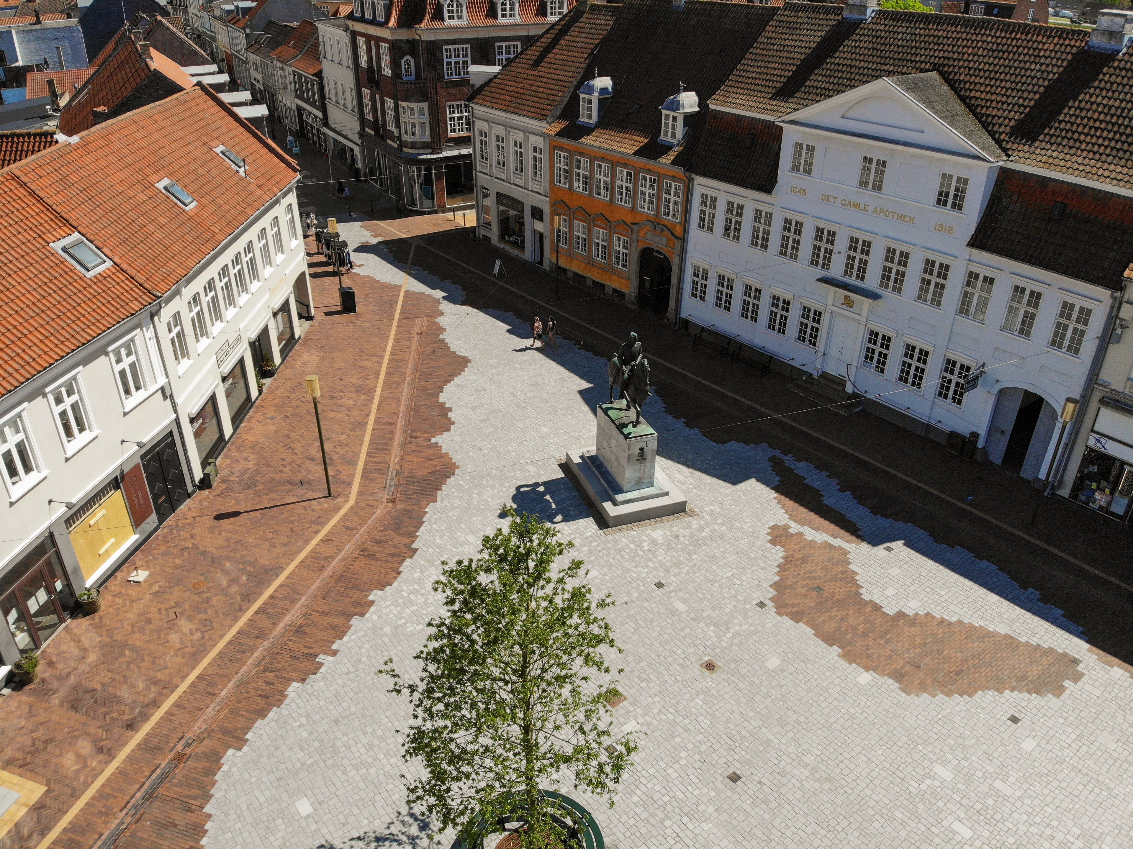 Luftfoto af Axeltorv i Nakskov med brostensbelægning, statue og historiske bygninger.