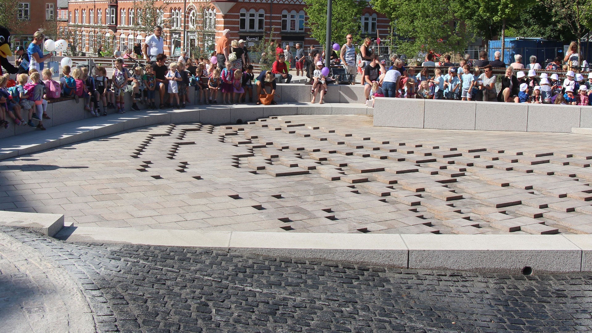 Ringsted Torv: Børn og voksne sidder ved et nyt, klimasikret torv med særlige stenbelægninger.