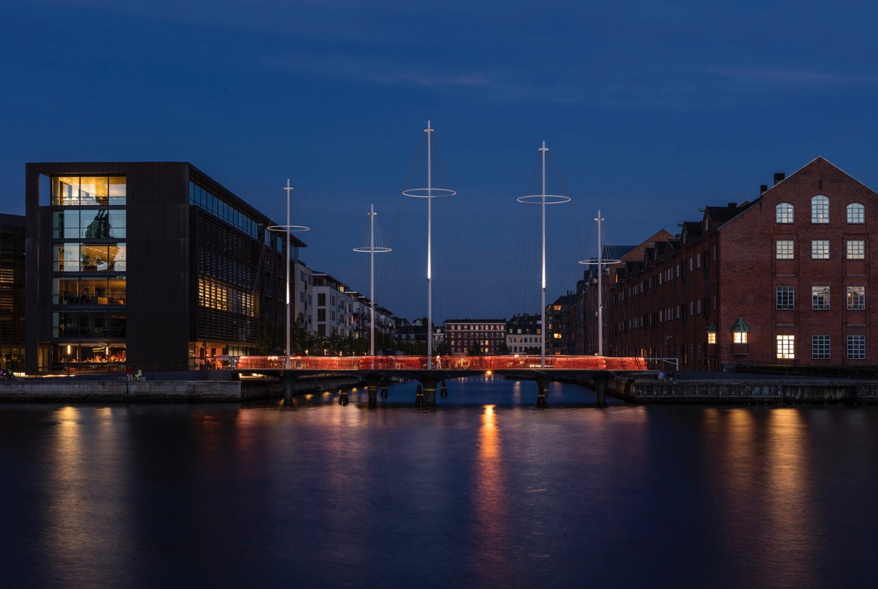 Cirkelbroen i København ved aftenstid med lysende master og refleksioner i vandet.