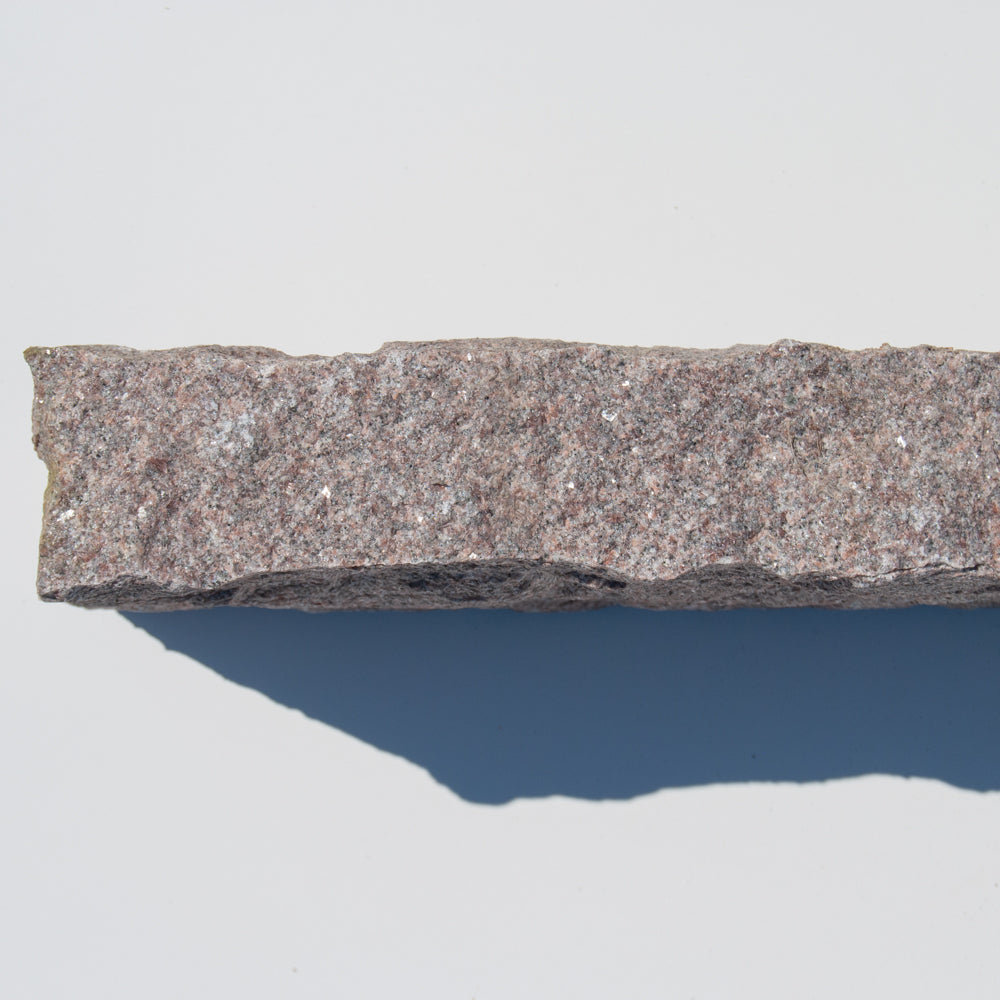 rød g352 granit kantsten med kløvet overflade, set fra siden.